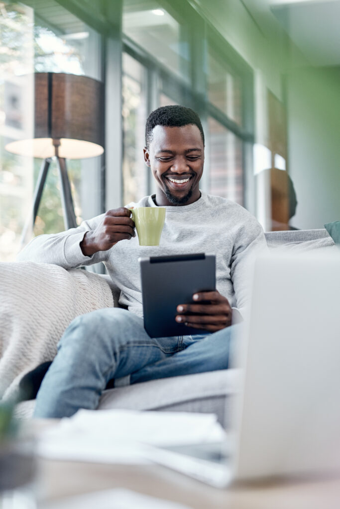 Shot of a young man using a digital tablet for virtual therapy in Ontario and having coffee on the sofa at home.